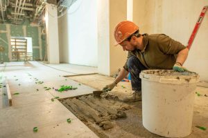 homme qui colle du carrelage dans une maison en construction